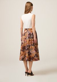 Gonna midi floreale marrone con finitura satinata, caratterizzata da motivi di fiori rosa e bianchi, abbinata a un top bianco aderente e tacchi neri.