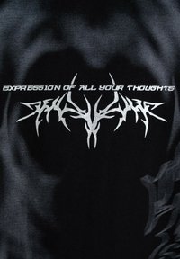 Czarna tkanina z białym napisem "WYRAŻENIE WSZYSTKICH TWOICH MYŚLI" nad abstrakcyjnym symetrycznym wzorem plemiennym.