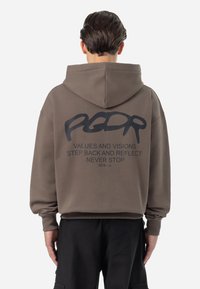 Sudadera marrón con una textura suave, presenta un gran gráfico negro en la espalda con texto y un logotipo en cursiva, terminado con capucha ajustable.