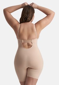 Body shaper beige con spalline regolabili e schiena scoperta. Texture liscia, design aderente e lunghezza fino a metà coscia con una leggera lucentezza.