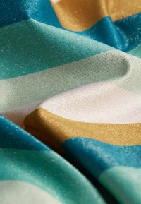 Tissu tissé avec un motif rayé turquoise, crème et or. Le matériau a une texture scintillante avec un léger éclat et des plis.