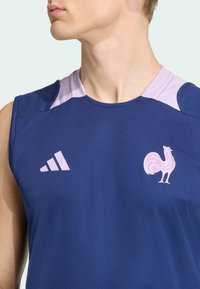 Mornarska atletska majica bez rukava s svijetloplavim naglascima. Sadrži Adidas logotip u ružičastoj boji i emblem pijetla. Lagana, glatka tkanina, bez rukava.