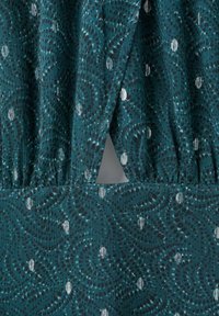 Teal tygklänning med ett texturerat mönster som har snurrande design och små metalliska detaljer, samlad vid midjan med en dold öppning.