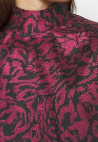 Haut à col haut avec une base noire présentant un motif floral texturé fuchsia et noir, combinant des couleurs vives et un design complexe.