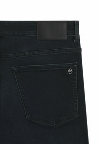 Jeans de mezclilla negra con una etiqueta de cuero que dice "BOSS", con un bolsillo trasero y un detalle de costura sutil. Tejido suave y texturizado.