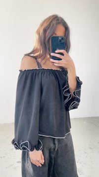 Sort off-the-shoulder bluse med flagrende lange ærmer, hvid flæsekant og en afslappet pasform. Bæres med mørke jeans.