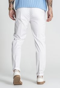 Weiße Baumwollchinos mit schmalem Schnitt, umgeschlagenen Säumen und seitlichen Taschen, kombiniert mit weißen Sneakern mit strukturierten Sohlen.