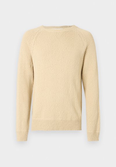 Pull texturé beige clair avec un col rond et des manches longues. Présente des poignets et un ourlet côtelés. Motif tissé visible sur toute la surface.