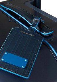 Marine leren bagagelabel met blauwe accenten. Beschikt over verticale ribbels, een gladde afwerking en een metalen identificatieplaat die met klinknagels is bevestigd.