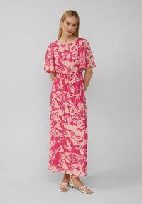 Robe maxi rose avec un motif floral dans des teintes plus claires. Manches fluides, taille élastique et coupe décontractée. Tissu lisse.
