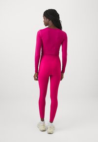 Set sportivo aderente in un vivace rosa, composto da una maglietta a maniche lunghe e leggings a vita alta, realizzato in materiale elastico con una texture liscia.