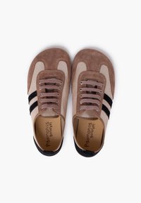 Un par de zapatos de ante marrón y beige con cordones, con rayas negras y plantillas de marca, vistos desde arriba sobre un fondo blanco.