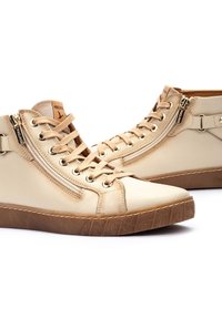 Sneakers alto beige in pelle, con cerniere metalliche, lacci piatti e suole in gomma testurizzata con un motivo geometrico.