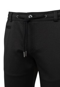Schwarze Hose mit Knopf- und Kordelzugbund, Metallösen, Gürtelschlaufen und einer Eingrifftasche auf der linken Seite.