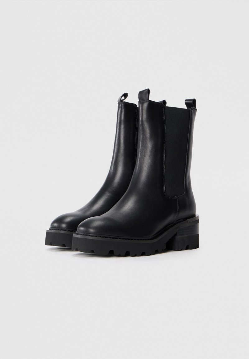 Botas de cuero negras hasta el tobillo con paneles laterales elásticos, punta redondeada y suela de goma gruesa. Cuenta con lengüetas para facilitar el uso.