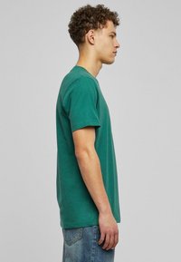 Zöld pamut póló, klasszikus kerek nyakkal, rövid ujjal, normál szabással. Egyszínű design, látható minták vagy kiegészítők nélkül. Kopott farmerral viselve.