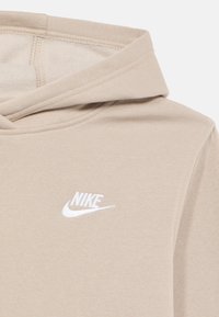Felpa con cappuccio beige in tessuto morbido con logo Nike bianco sul petto, cappuccio con coulisse e dettagli di cuciture visibili.