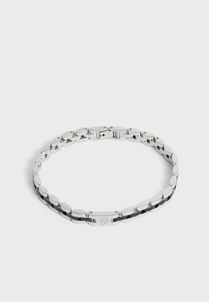 Bracelet chaîne en métal ton argenté avec des maillons ovales et un fermoir rectangulaire décoré d'un motif gravé, présenté sur fond blanc.