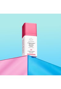 White cylindrical bottle with a pink cap, labeled "A-Shaba Complex Eye Serum," resting on pink and blue geometric surfaces.