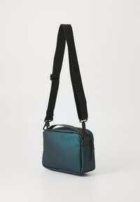 Borsa a tracolla verde acqua con una superficie liscia, dotata di una tracolla nera regolabile, una maniglia superiore e una forma rettangolare. Design minimalista.