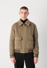 Braune Fischgrätjacke mit Reißverschluss, großen Fronttaschen und geripptem Saum. Verfügt über einen Kragen und eine weiche Textur.
