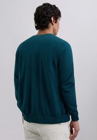 Pulover tricotat teal, cu mâneci lungi, decolteu rotund și tiv cu nervuri. Textură netedă și design minimalist, evidențiind o culoare solidă fără modele.
