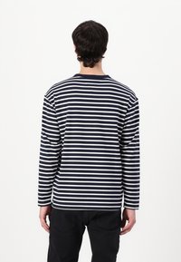 Langermet skjorte i marineblå og hvite striper med rund hals og avslappet passform, laget av mykt bomullsmateriale. Minimalistisk design, uten mønstre.