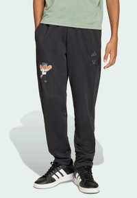 Černé tepláky vyrobené z hladké tkaniny s potiskem postavy z Minecraftu na levé nohavici a akcenty loga Adidas.