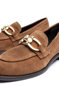 Mocassini in suede marrone con dettaglio della fibbia dorata e suola in gomma nera. Presentano una texture liscia e un design classico senza lacci.