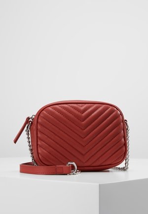 Czerwona skórzana torebka na ramię z pikowaniem w kształcie litery V, zamkiem błyskawicznym na górze i regulowanym łańcuszkowym paskiem. Charakteryzuje się gładką fakturą i kompaktowym kształtem.