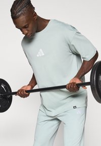 Ανοιχτό πράσινο βαμβακερό μπλουζάκι με λευκό λογότυπο adidas στην αριστερή πλευρά, συνδυασμένο με παντελόνια στο ίδιο ανοιχτό πράσινο χρώμα.