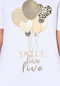 Camiseta blanca de tela con un diseño de globos multicolores y patrones, detalles dorados, y el texto "SMILE love live" en letras decorativas.