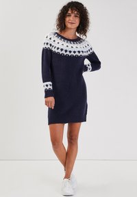 Robe tricotée bleu marine avec un empiècement et des manches à motifs blancs. Dotée d'un ourlet et de poignets côtelés, elle offre une coupe décontractée. Assortie à des baskets blanches.