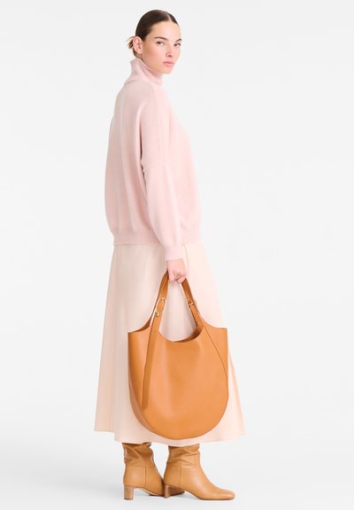 Braune Leder-Tasche in geschwungener Form, mit verstellbarem Tragegurt, glatter Textur, kombiniert mit einem hellrosa gestrickten Pullover und einem fließenden Rock.