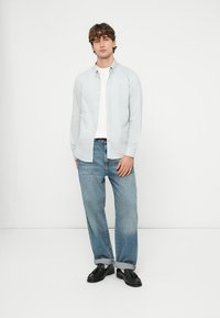 Jasnoniebieska koszula na guziki, pod spodem biała koszulka, zestawiona z luźnymi niebieskimi dżinsami podwiniętymi przy mankietach oraz czarnymi butami.