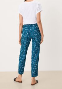 Teal, bloemenpatroon broek met een relaxte pasvorm en elastische tailleband, gecombineerd met een witte cropped t-shirt en zwarte platte sandalen.