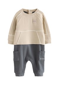 Beige top med raglanærmer og et rektangulært mærke med teksten "BAKER"; kombineret med grå bukser med sidelommer og trykknapslukning.