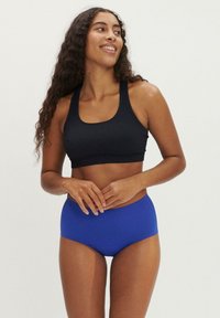 Svart sportig crop top med fyrkantig halsringning, tillsammans med högmidjade blå shorts. Materialet verkar elastiskt, slätt och figursytt.