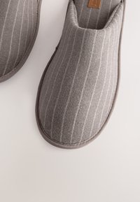 Chaussons gris en tissu doux et texturé avec des rayures blanches verticales, dotés d'un bout arrondi et d'un bord contrastant autour des ouvertures.