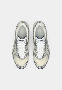 Beżowe sportowe buty z siateczki z srebrnymi akcentami, posiadające biały design na sznurowadła i wyściełany język. Charakterystyczne logo marki na boku.