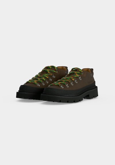 Paire de chaussures de randonnée marron avec semelles épaisses noires et lacets rayés verts, jaunes et rouges sur fond blanc.