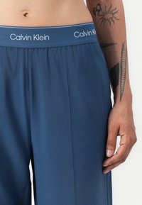 Calvin Klein marineblå treningbukser med elastisk midje, inneholder en logo. Glatt tekstur og synlige sidelommer.