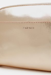Pochette cosmetica in oro rosa metallico con una finitura liscia, caratterizzata da un logo in rilievo discreto e da una delicata cucitura lungo la cucitura.