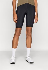 Svarte sykkelshorts med en tettsittende design, som har en glatt tekstur og kontrasterende svarte mansjetter. Båret med hvite sokker og sko.