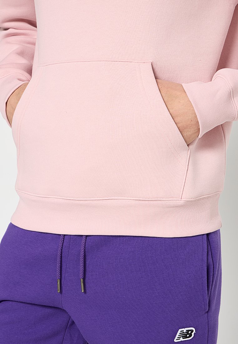 Sweatshirt rose clair avec une poche frontale et des poignets côtelés, associé à un pantalon de survêtement violet arborant un logo brodé.