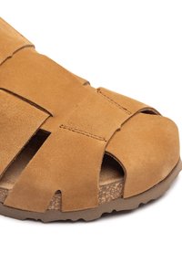 Sandalo in suede beige con ampie cinghie incrociate, design aperto sulla punta, soletta in sughero texturizzato e suola in gomma flessibile con leggera grip.