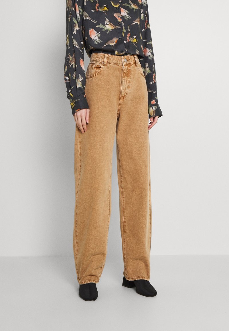 Beige vida jeans i denim, med hög midja, framfickor och en subtil textur. Tillsammans med en mörk mönstrad topp.