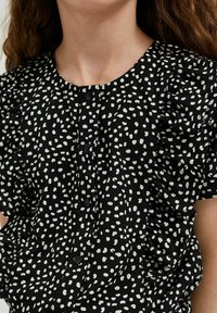 Czarna bluzka w białe kropki, okrągły dekolt, zapięcie na guziki oraz krótkie falbaniaste rękawy, wykonana z lekkiego materiału.