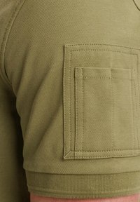 Olivi vihreä lyhythihainen paita, jossa on teksturoitu kangas, sisältäen rintataskun hihassa ja ribattu helma vyötäröllä.