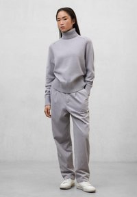 Suéter de cuello alto gris claro con bordes acanalados, combinado con pantalones anchos gris claro y zapatillas blancas. Textura suave, diseño casual.